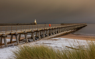 Fototapeta na wymiar A freezing, snowy morning at Blyth beach, looking across the sand dunes and marram grass towards the old wooden Pier