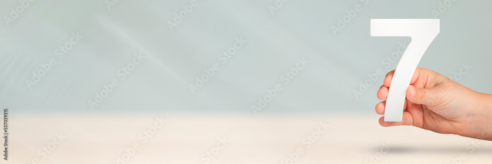 Poster number seven in hand. hand holding white number 7 on blurred background with copy space. concept wit