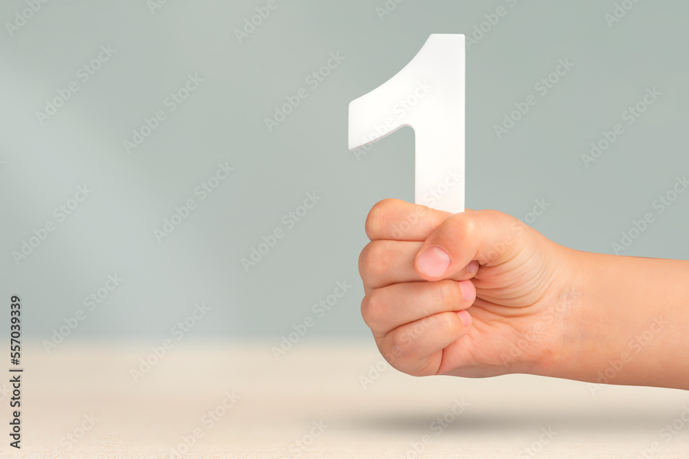 Poster number one in hand. a hand holds a white number one on a blurred background with copy space. concept
