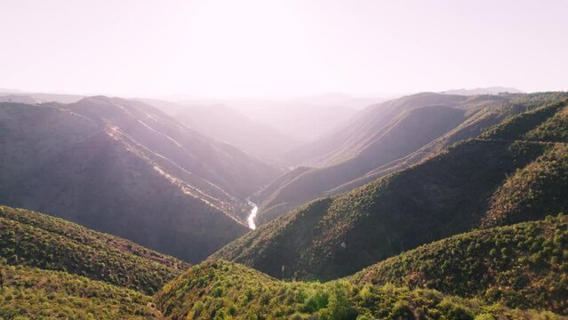 Dramatic Aerial shot over valley with river far below. Shot at sunrise with bright dazzling light and lens flare.