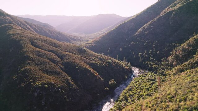 Aerial flying through a valley with a river running below. Shot in California Sierras during summer.