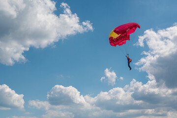 Parachutist paraglider on a yellow-red wing in a blue sky with clouds. Extreme sports and hobbies.