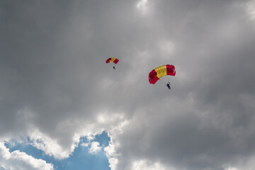 Parachutist paraglider on a yellow-red wing in a blue sky with clouds. Extreme sports and hobbies.
