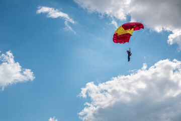 Parachutist paraglider on a yellow-red wing in a blue sky with clouds. Extreme sports and hobbies.