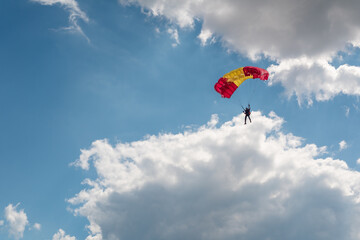 Parachutist paraglider on a yellow-red wing in a blue sky with clouds. Extreme sports and hobbies.