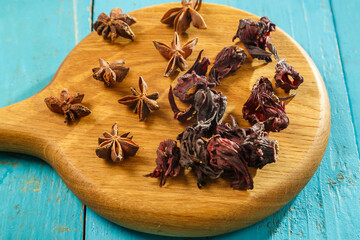 Hibiscus flowers and star anise on a wooden board on a blue table.