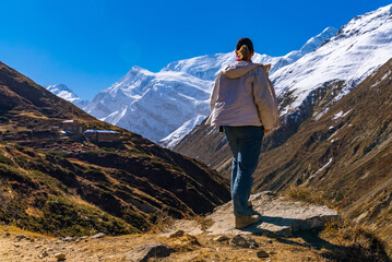 Female trekker looking at view of small tea houses and snowy mountain peaks on the Annapurna Circuit Trek