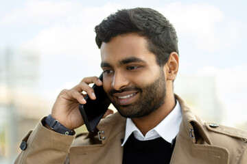 Portrait of handsome smiling Indian man talking on mobile phone on the street. Technology concept 