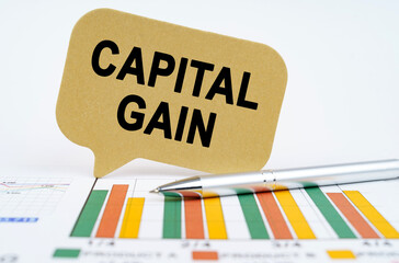 On the financial charts lies a pen and a sign with the inscription - capital gain