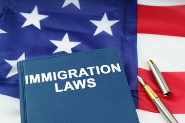 On the US flag lies a pen and a book with the inscription - IMMIGRATION LAWS
