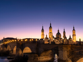 Fototapeta na wymiar View of the basilica del Pilar de Zaragoza with the medieval stone bridge over the Ebro river in the foreground during sunset in winter.