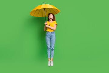Full size photo of excited cheerful girl jumping arms hold umbrella isolated on green color background