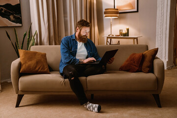 Smiling man using laptop while sitting on couch in cozy living room
