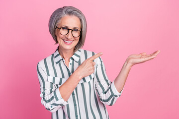 Photo of old pensioner businesswoman wear striped shirt hold palm direct finger empty space high quality product isolated on pink color background