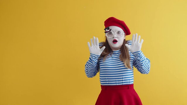 Female mime shows fright, a threat to life. Young actress woman in white-faced , wearing beret and a striped T-shirt, will raise her hands in front of her fright. Concept of fear