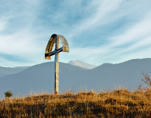 Wooden cross on autumn misty mountain slope.
