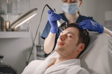 Young man in cosmetologist cabinet has a face procedure of cavitation - obrazy, fototapety, plakaty