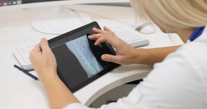 Holding a tablet with x-rays of a pet in his hands, the veterinarian leads his finger across the screen, studying the picture. The veterinarian carefully examines the dog's x-ray to make a diagnosis.
