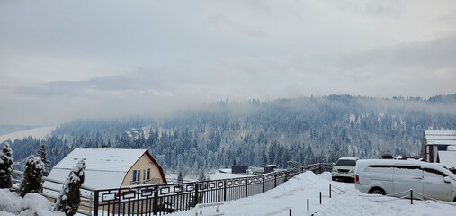 village in the mountains and snow-covered forest in the fog. enjoying the beauty of nature while on vacation or traveling. winter forest with coniferous trees