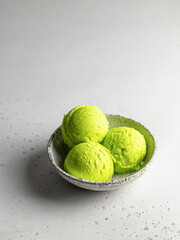 Pistachio ice cream scoop in bowl on gray textured background with text space