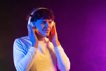 Handsome man listening music with headphones on gradient neon background. Stylish student guy...