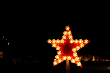Selective focus view at red star decorated sign surround the outline with line of light bulbs on dark background. 