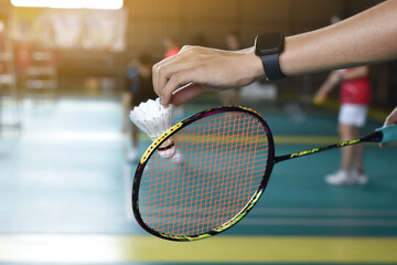 Badminton racket and old white shuttlecock holding in hands of player while serving it over the net...