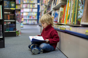 Cute blond toddler child, boy, reading book in a book store