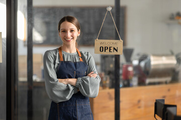 Young american businesswoman small business owner standing at cafeteria door entrance pen signboard, A cheerful entrepreneur young waitress in a blue apron near the glass door 