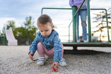 Fototapeta premium One girl small caucasian child female toddler 18 months old in park play in day by speedy spinner merry-go-round turnabout childhood and growing up concept copy space