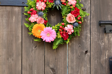 Fototapeta na wymiar アンティークな木製アーチ扉に飾られた花のリーリース　生花を使った華やかなフラワーアレンジメント　手作りの花のリース