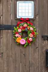 Fototapeta na wymiar アンティークな木製アーチ扉に飾られた花のリーリース　生花を使った華やかなフラワーアレンジメント　手作りの花のリース