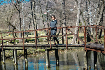 Beautiful young blonde woman stands by a wooden fence on a lake in early spring