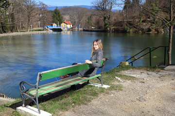 Beautiful young woman is sitting on a bench by the lake
