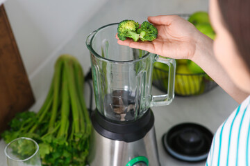 Woman adding broccoli into blender for smoothie in kitchen, closeup