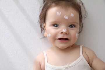 Cute little baby with cream on face in comfortable crib, top view. Space for text