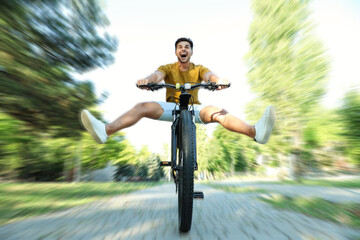 Handsome young man riding bicycle in city park, low angle view. Motion blur effect