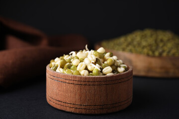 Wooden bowl with sprouted green mung beans on black background, closeup