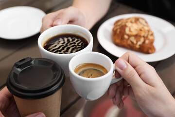 Friends drinking coffee at wooden table in outdoor cafe, closeup