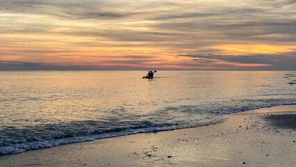 Fototapeta premium people paddling the shore of the ocean at sunset