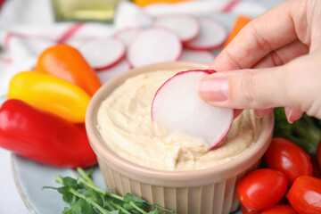 Woman dipping slice of radish into hummus at table, closeup