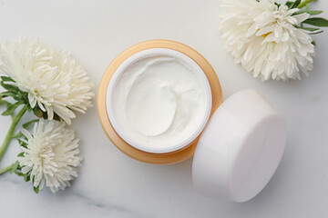 Obraz na płótnie Canvas Jar of face cream and flowers on white marble table, flat lay