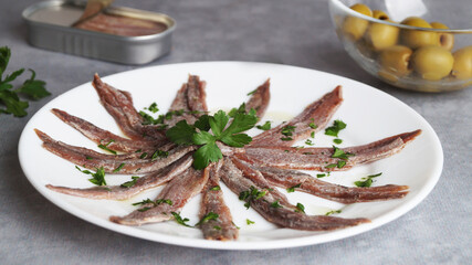 Plate with anchovy fillets and parsley on grey table