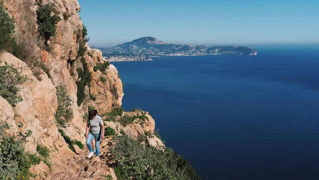 Women tourists climbing on rocky mountain Penon de Ifach, Calpe, Spain