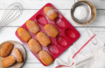 Delicious madeleine cookies and baking mold on white wooden table, flat lay