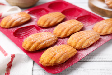 Delicious madeleine cookies in baking mold on white wooden table, closeup