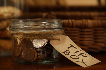 Tip box full of coins on wooden table in cafe, closeup