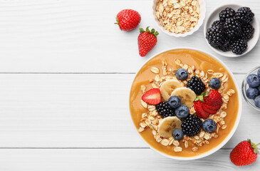 Delicious smoothie bowl with fresh berries, banana and oatmeal on white wooden table, flat lay. Space for text
