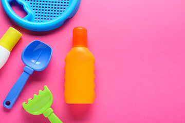 Bottle of suntan cream and children's beach toys on pink background, flat lay. Space for text