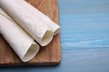 Delicious rolled Armenian lavash on light blue wooden table, space for text